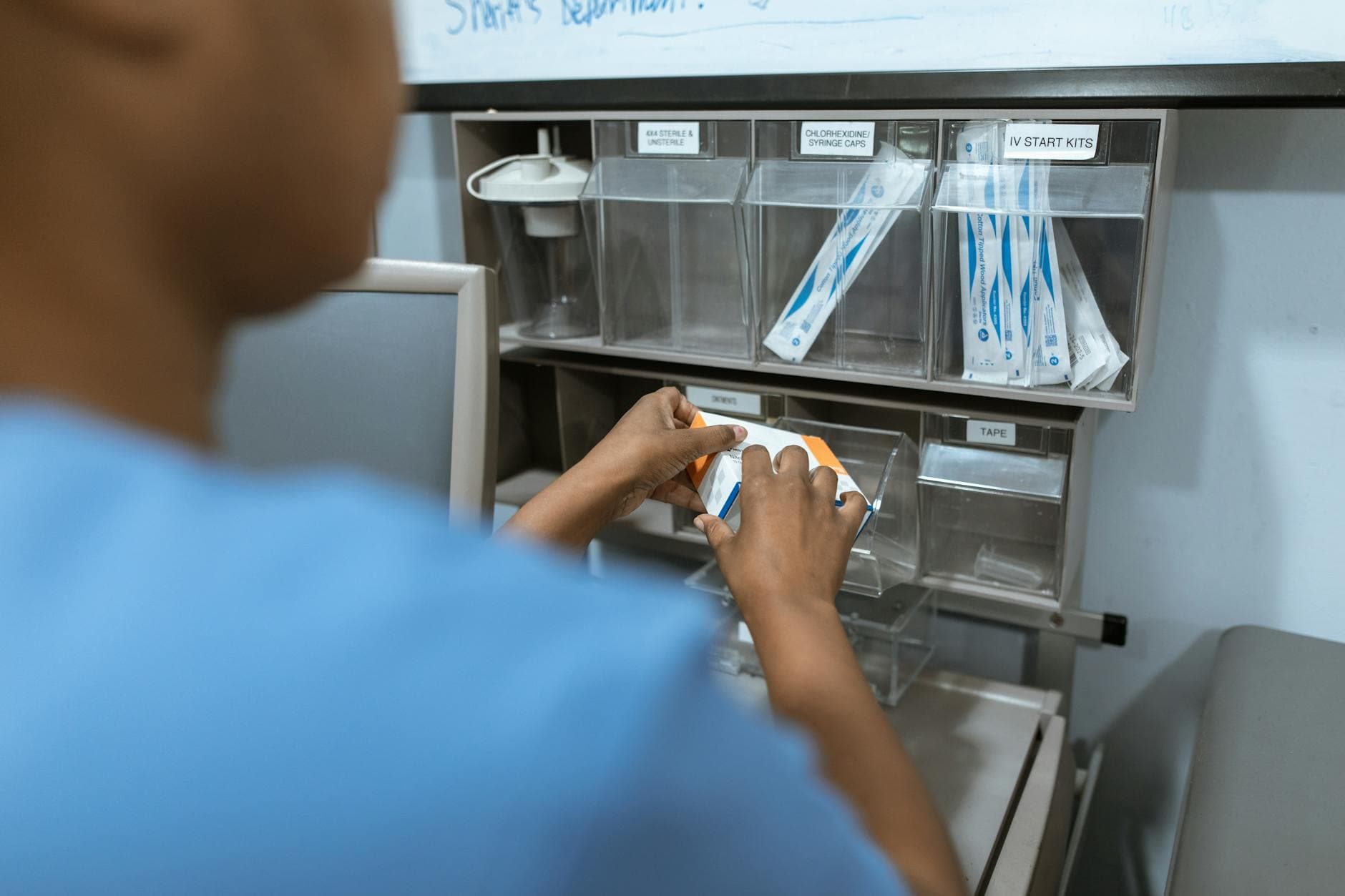 A nurse organizes medical supplies in a hospital setting. Focus on hands and storage unit with IV kits.